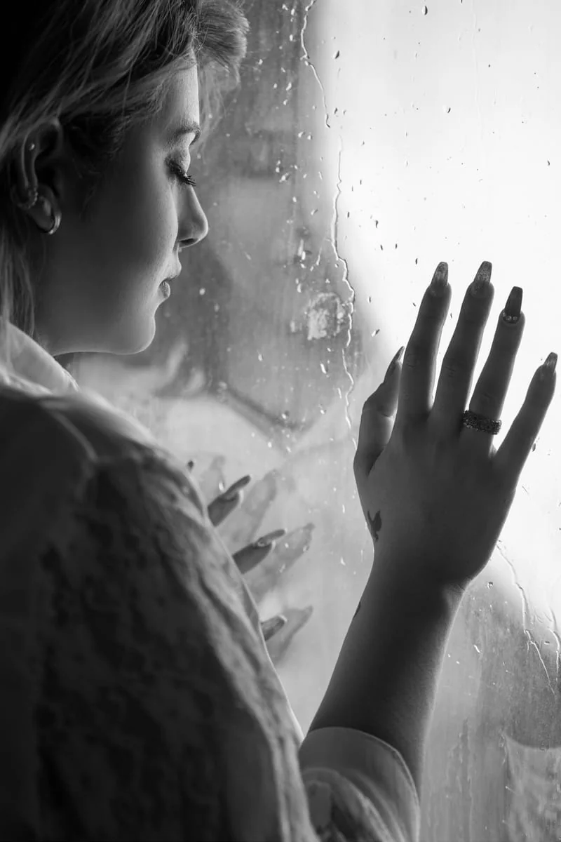 Mujer pensativa frente a una ventana con lluvia, reelaborando una ruptura