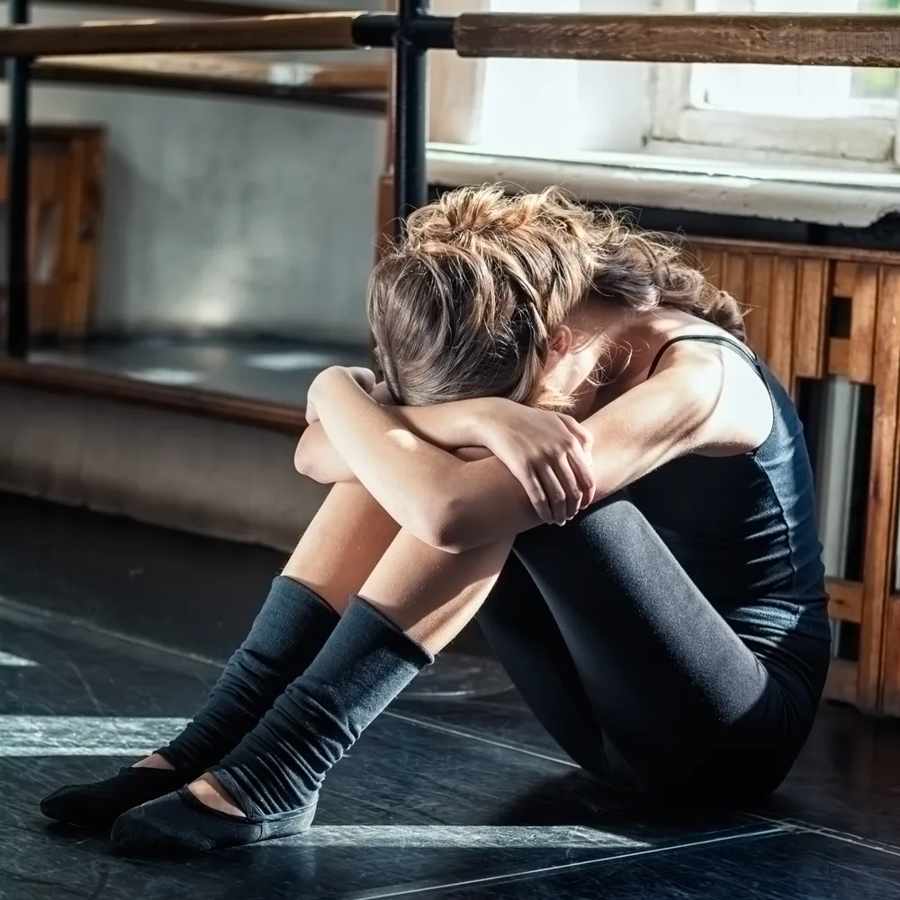 Adolescente sentada en el suelo con la cabeza apoyada en las rodillas